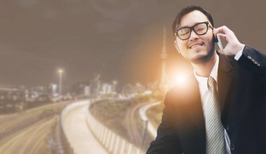 Genç işadamı istimal hareket eden telefon ile modern şehir binaları arka plan.