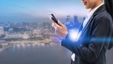 Cep telefonu ile modern şehir binaları arka plan kullanarak genç iş kadını. Gelecekteki telekomünikasyon teknolojisi ve internet şeyler (çok) kavramının.