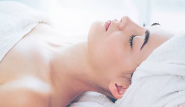 Spa yatağında uzanan rahat genç bir kadın lüks bir spa merkezinde yüz bakımı ve masaj için hazırlandı. Sağlık, stres atma ve gençleştirme kavramı.