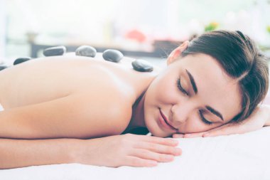 Kadın kaplıca salonunda profesyonel güzellik terapisti tarafından sıcak taş masajı görüyor. Lüks sağlık, sırt stresi ve gençleştirme kavramı..