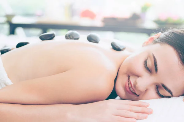Woman getting hot stone massage treatment by professional beautician therapist in spa salon. Luxury wellness, back stress relief and rejuvenation concept.