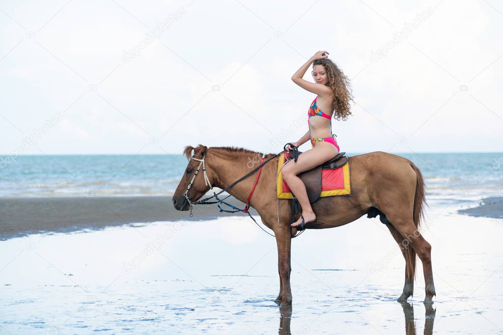 Woman fashion model riding a horse on the beach in summer. Luxury travel vacation.