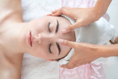 Lüks bir spa merkezinde masaj terapisti tarafından yüz masajı ve spa tedavisi için kaplıcaya uzanmış rahat bir kadın. Sağlık, stres atma ve gençleştirme kavramı.