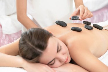 Kadın kaplıca salonunda profesyonel güzellik terapisti tarafından sıcak taş masajı görüyor. Lüks sağlık, sırt stresi ve gençleştirme kavramı..