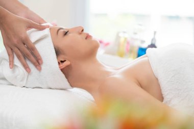 Spa yatağında uzanan rahat genç bir kadın lüks bir spa merkezinde yüz bakımı ve masaj için hazırlandı. Sağlık, stres atma ve gençleştirme kavramı.