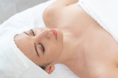 Spa yatağında uzanan rahat genç bir kadın lüks bir spa merkezinde yüz bakımı ve masaj için hazırlandı. Sağlık, stres atma ve gençleştirme kavramı.