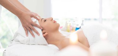 Lüks bir spa merkezinde masaj terapisti tarafından yüz masajı ve spa tedavisi için kaplıcaya uzanmış rahat bir kadın. Sağlık, stres atma ve gençleştirme kavramı.
