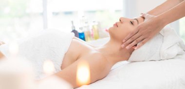 Lüks bir spa merkezinde masaj terapisti tarafından yüz masajı ve spa tedavisi için kaplıcaya uzanmış rahat bir kadın. Sağlık, stres atma ve gençleştirme kavramı.
