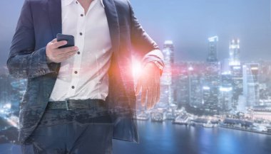 Genç işadamı cep telefonunuzun ve modern şehir binaları arka plan ile. Gelecekteki telekomünikasyon teknolojisi ve internet şeyler (çok) kavramının.