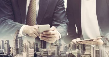 Cep telefonu ile modern şehir binaları arka plan kullanarak genç iş adamları. Gelecekteki telekomünikasyon teknolojisi ve internet şeyler (çok) kavramının.