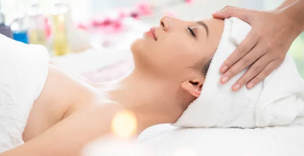 Relaxed woman lying on spa bed for facial and head massage spa treatment by massage therapist in a luxury spa resort. Wellness, stress relief and rejuvenation concept.