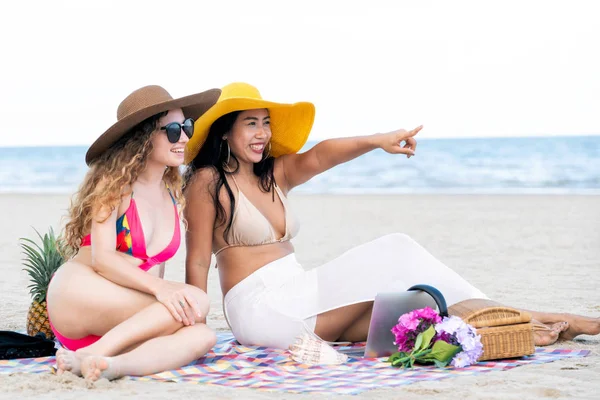 Mutlu birlikte tropikal kum üzerine oturan bikinili kadınlar yaz tatil plaj. Seyahat yaşam tarzı.