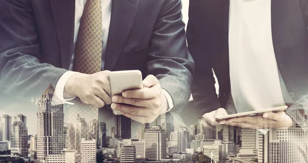 Cep telefonu ile modern şehir binaları arka plan kullanarak genç iş adamları. Gelecekteki telekomünikasyon teknolojisi ve internet şeyler (çok) kavramının.