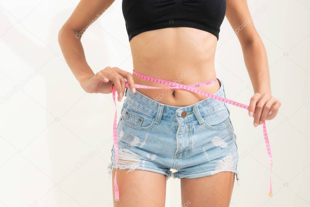 Young slim woman measures her waist by measuring tape after diet against white backgrounds. Concept of weight loss success.