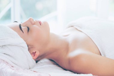Spa yatağında uzanan rahat genç bir kadın lüks bir spa merkezinde yüz bakımı ve masaj için hazırlandı. Sağlık, stres atma ve gençleştirme kavramı.