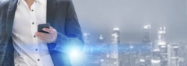 Genç işadamı cep telefonunuzun ve modern şehir binaları arka plan ile. Gelecekteki telekomünikasyon teknolojisi ve internet şeyler (çok) kavramının.