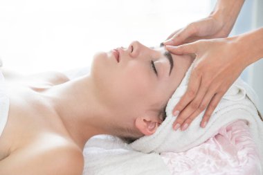 Lüks bir spa merkezinde masaj terapisti tarafından yüz masajı ve spa tedavisi için kaplıcaya uzanmış rahat bir kadın. Sağlık, stres atma ve gençleştirme kavramı.