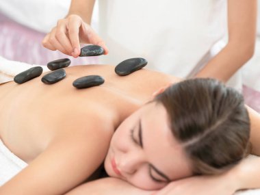 Kadın kaplıca salonunda profesyonel güzellik terapisti tarafından sıcak taş masajı görüyor. Lüks sağlık, sırt stresi ve gençleştirme kavramı..