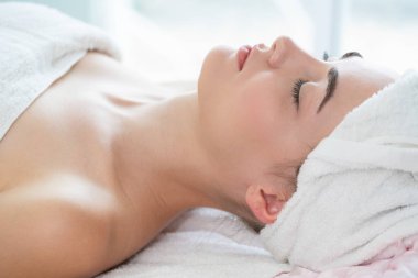 Spa yatağında uzanan rahat genç bir kadın lüks bir spa merkezinde yüz bakımı ve masaj için hazırlandı. Sağlık, stres atma ve gençleştirme kavramı.