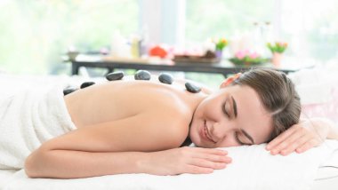 Kadın kaplıca salonunda profesyonel güzellik terapisti tarafından sıcak taş masajı görüyor. Lüks sağlık, sırt stresi ve gençleştirme kavramı..