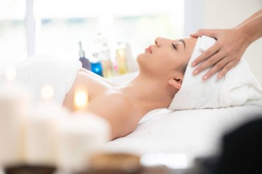 Lüks bir spa merkezinde masaj terapisti tarafından yüz masajı ve spa tedavisi için kaplıcaya uzanmış rahat bir kadın. Sağlık, stres atma ve gençleştirme kavramı.