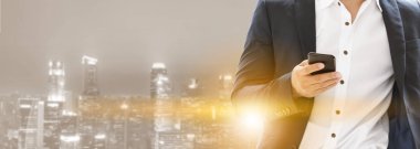 Genç işadamı cep telefonunuzun ve modern şehir binaları arka plan ile. Gelecekteki telekomünikasyon teknolojisi ve internet şeyler (çok) kavramının.