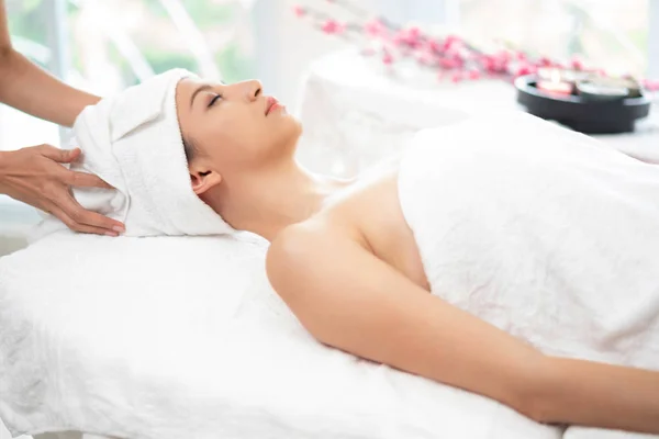 Relaxed young woman lying on spa bed prepared for facial treatment and massage in luxury spa resort. Wellness, stress relief and rejuvenation concept.