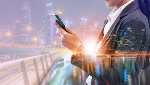 Cep telefonu ile modern şehir binaları arka plan kullanarak genç iş kadını. Gelecekteki telekomünikasyon teknolojisi ve internet şeyler (çok) kavramının.