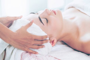 Lüks bir spa merkezinde masaj terapisti tarafından yüz masajı ve spa tedavisi için kaplıcaya uzanmış rahat bir kadın. Sağlık, stres atma ve gençleştirme kavramı.