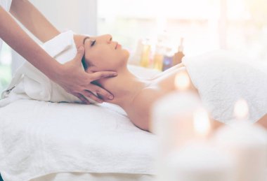 Lüks bir spa merkezinde masaj terapisti tarafından yüz masajı ve spa tedavisi için kaplıcaya uzanmış rahat bir kadın. Sağlık, stres atma ve gençleştirme kavramı.