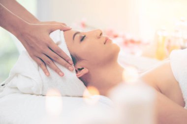 Lüks bir spa merkezinde masaj terapisti tarafından yüz masajı ve spa tedavisi için kaplıcaya uzanmış rahat bir kadın. Sağlık, stres atma ve gençleştirme kavramı.