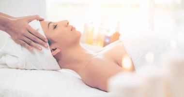 Lüks bir spa merkezinde masaj terapisti tarafından yüz masajı ve spa tedavisi için kaplıcaya uzanmış rahat bir kadın. Sağlık, stres atma ve gençleştirme kavramı.