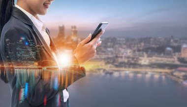 Cep telefonu ile modern şehir binaları arka plan kullanarak genç iş kadını. Gelecekteki telekomünikasyon teknolojisi ve internet şeyler (çok) kavramının.