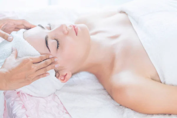 Relaxed woman lying on spa bed for facial and head massage spa treatment by massage therapist in a luxury spa resort. Wellness, stress relief and rejuvenation concept.