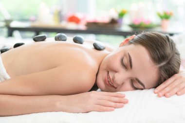 Kadın kaplıca salonunda profesyonel güzellik terapisti tarafından sıcak taş masajı görüyor. Lüks sağlık, sırt stresi ve gençleştirme kavramı..