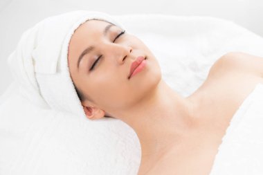 Spa yatağında uzanan rahat genç bir kadın lüks bir spa merkezinde yüz bakımı ve masaj için hazırlandı. Sağlık, stres atma ve gençleştirme kavramı.