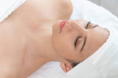 Spa yatağında uzanan rahat genç bir kadın lüks bir spa merkezinde yüz bakımı ve masaj için hazırlandı. Sağlık, stres atma ve gençleştirme kavramı.