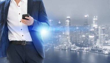 Genç işadamı cep telefonunuzun ve modern şehir binaları arka plan ile. Gelecekteki telekomünikasyon teknolojisi ve internet şeyler (çok) kavramının.