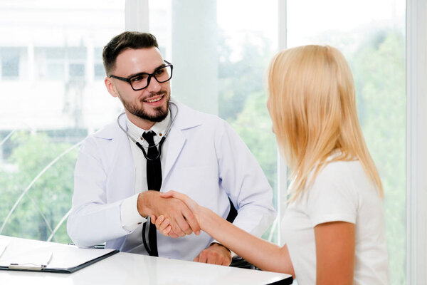 Мужчина-врач пожимает руку пациентке в больничном кабинете. Здравоохранение и медицинское обслуживание
.