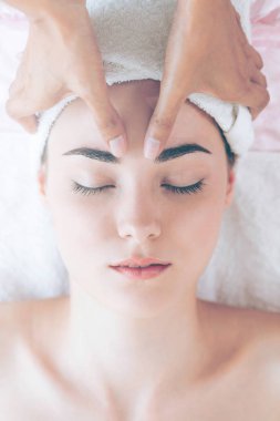 Lüks bir spa merkezinde masaj terapisti tarafından yüz masajı ve spa tedavisi için kaplıcaya uzanmış rahat bir kadın. Sağlık, stres atma ve gençleştirme kavramı.