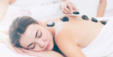 Kadın kaplıca salonunda profesyonel güzellik terapisti tarafından sıcak taş masajı görüyor. Lüks sağlık, sırt stresi ve gençleştirme kavramı..