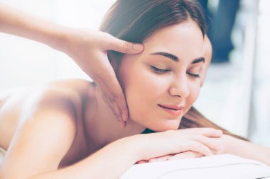 Lüks bir spa merkezinde masaj terapisti tarafından yüz masajı ve spa tedavisi için kaplıcaya uzanmış rahat bir kadın. Sağlık, stres atma ve gençleştirme kavramı.
