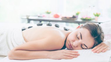 Kadın kaplıca salonunda profesyonel güzellik terapisti tarafından sıcak taş masajı görüyor. Lüks sağlık, sırt stresi ve gençleştirme kavramı..