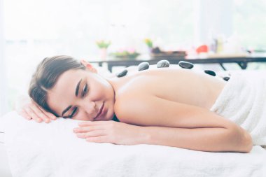 Kadın kaplıca salonunda profesyonel güzellik terapisti tarafından sıcak taş masajı görüyor. Lüks sağlık, sırt stresi ve gençleştirme kavramı..