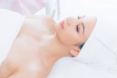 Spa yatağında uzanan rahat genç bir kadın lüks bir spa merkezinde yüz bakımı ve masaj için hazırlandı. Sağlık, stres atma ve gençleştirme kavramı.