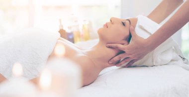 Lüks bir spa merkezinde masaj terapisti tarafından yüz masajı ve spa tedavisi için kaplıcaya uzanmış rahat bir kadın. Sağlık, stres atma ve gençleştirme kavramı.