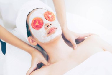 Beautiful woman having a facial mask treatment with tomato cream extract showing benefit of nature treatment. Anti-aging cosmetology, facial skin care and luxury lifestyle concept. clipart