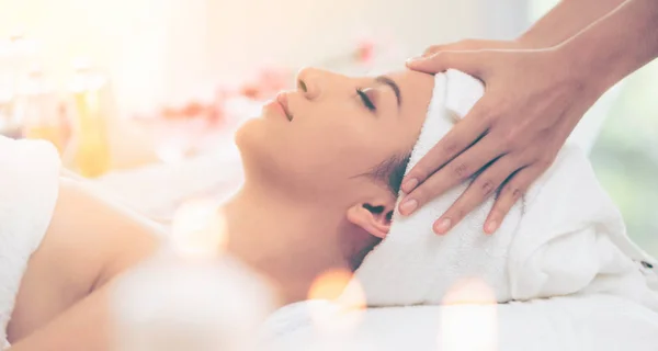 Relaxed woman lying on spa bed for facial and head massage spa treatment by massage therapist in a luxury spa resort. Wellness, stress relief and rejuvenation concept.