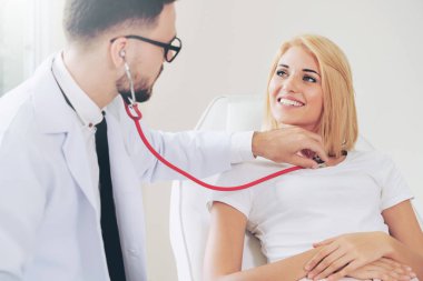 Erkek doktor konuşuyor ve Bayan hasta hastane ofisinde inceleyerek. Sağlık ve tıbbi hizmet.