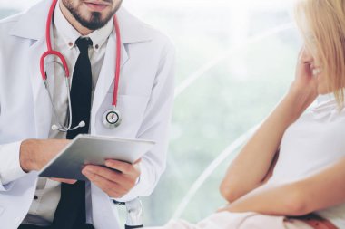 Erkek doktor konuşuyor ve Bayan hasta hastane ofisinde inceleyerek. Sağlık ve tıbbi hizmet.